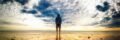 A lone figure stands on a tranquil beach during a vivid sunset, reflecting on the wet sand.
